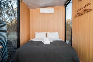 A modern bedroom with a large bed, wooden walls, and a view of trees through a window.