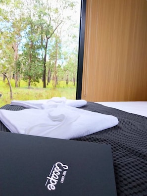 A room with a view of trees through a window, a black mat, and a towel on a bed.