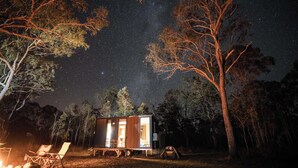 Uma cabana pequena com vista desimpedida do céu noturno, rodeada por árvores.
