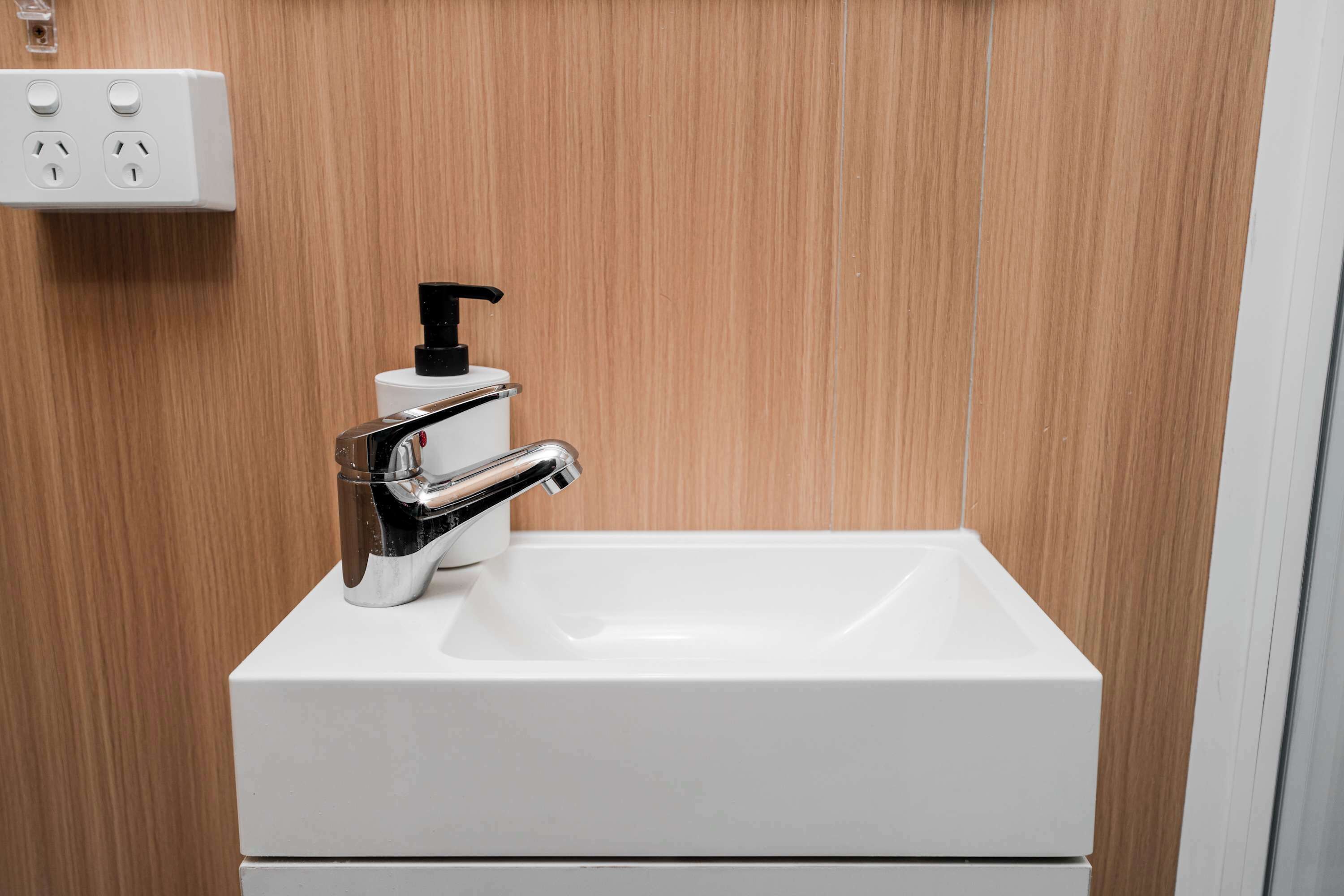 Ein weißes Waschbecken mit chromfarbenem Wasserhahn und einem schwarzen Seifenspender.