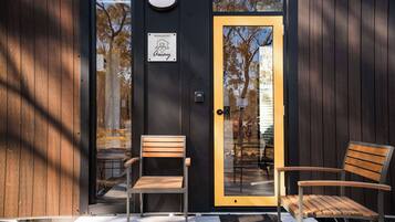 A modern building entrance with a glass door, two wooden chairs outside, and a 'Managed by Tiny Away' sign.
