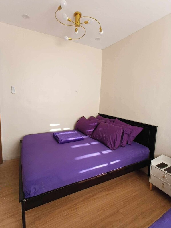 A bedroom with a bed, a nightstand, a wall-mounted light fixture, and a wooden floor.