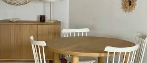 Un comedor con una mesa redonda de madera, sillas blancas, un aparador de madera y dos espejos decorativos colgantes.