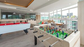 A modern indoor space with a foosball table, seating area, and large windows. - CoWorking Pool-Gym-Game Room+Cinema the city C220 (Tambon Wichit)