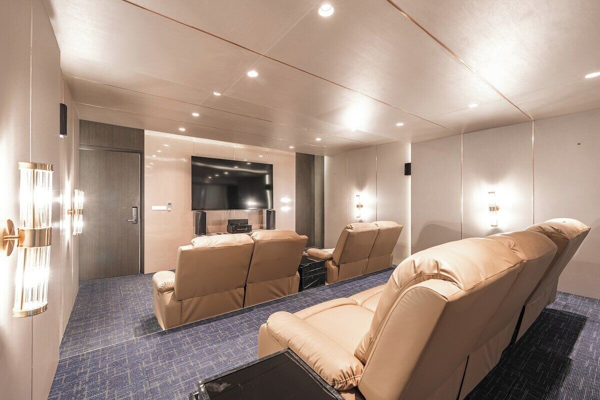 Une chambre d’hôtel moderne dotée d’un grand téléviseur à écran plat, de canapés en cuir beige et d’un tapis à motifs bleus.