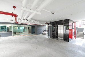 Un hall d’entrée spacieux au design moderne, comprenant une cloison en verre, un mur d’accent aux couleurs rouge et noir, et des tuyaux apparents au plafond.