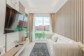 Ein modernes Wohnzimmer mit Flachbildfernseher, einer Couch, einem Couchtisch und Blick auf eine Stadtlandschaft durch große Fenster.