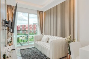 Un salon moderne avec un canapé, un téléviseur à écran plat, une grande fenêtre avec des rideaux et une vue sur les bâtiments environnants.