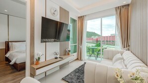 A modern hotel room with a bed, a TV, a sofa, a small table, and a window with a view of buildings. - CoWorking Pool-Gym-Game Room+Cinema the city C220 (Tambon Wichit)