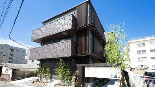 A multi-story building with a modern design, featuring a mix of brick and wood paneling, and a small garden area with young trees.