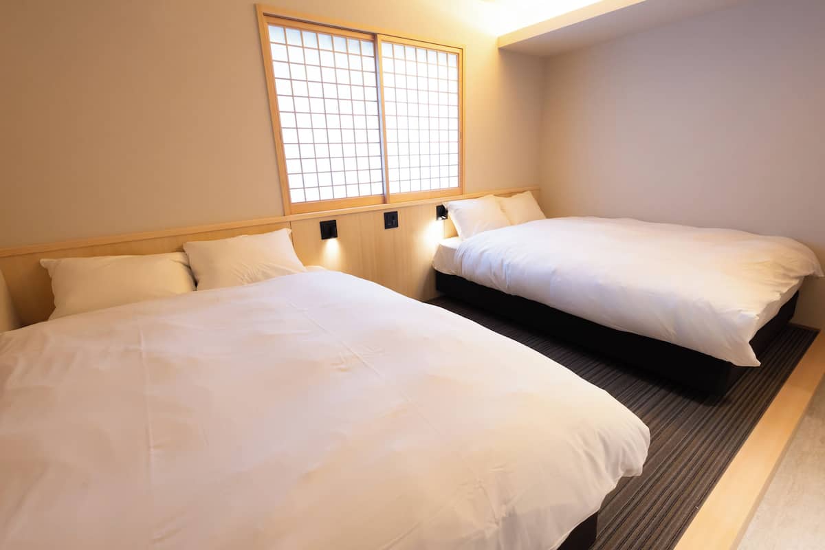 A hotel room with two beds, a window with a grid pattern, and a carpeted floor.