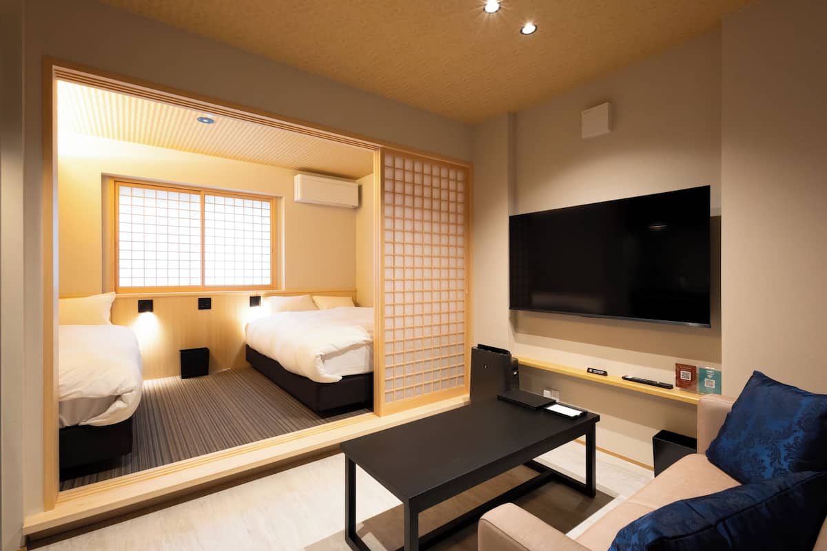 A hotel room with two beds, a TV, a coffee table, and a sliding door.