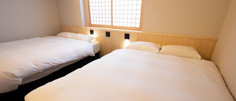 A room with two beds, a window with a grid pattern, and wall-mounted lights.