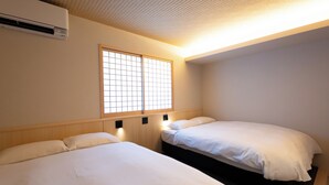 A hotel room with two beds, a window with a grid pattern, and an air conditioning unit.