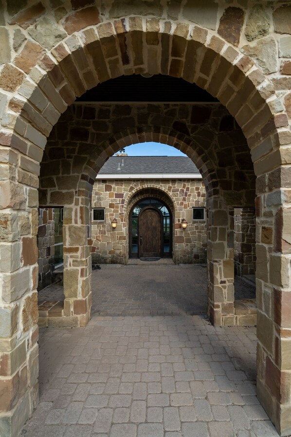 Una entrada de piedra en arco que conduce a un edificio con puerta de madera y un sendero de ladrillo.
