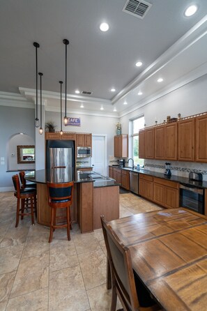 A modern kitchen with a central island, wooden cabinets, stainless steel appliances, and pendant lighting.