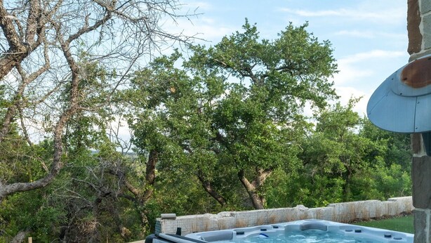 A hot tub in a backyard with a stone wall, trees, and a clear sky.