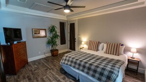 A bedroom with a bed, a dresser, a ceiling fan, a potted plant, and a television.