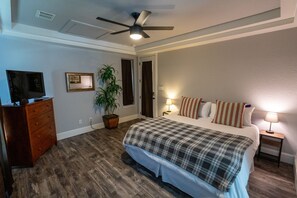 A bedroom with a bed, a dresser, a ceiling fan, a potted plant, and a television.