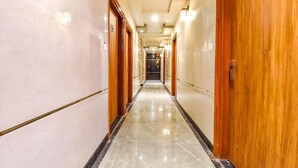 A hotel hallway with marble floors, wooden doors, and a central light fixture. - Hotel KPL (Jaipur)