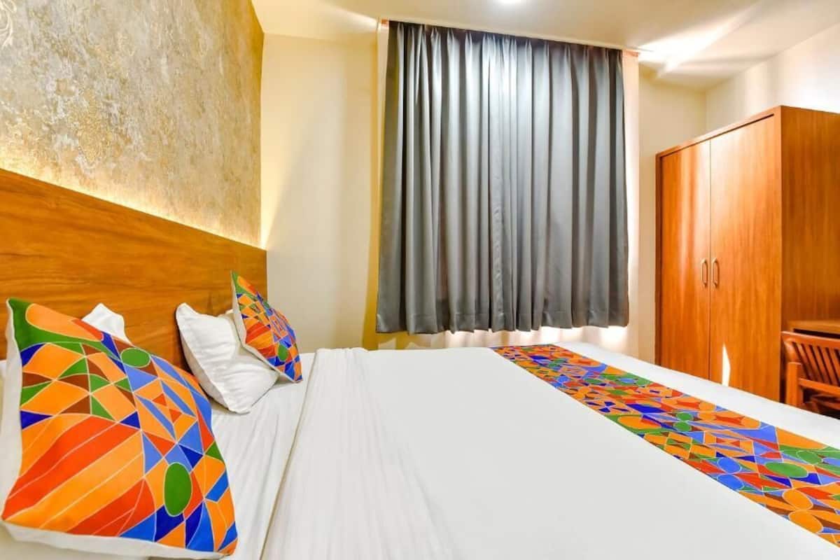 A hotel room with a bed, a wooden wardrobe, a window with curtains, and a colorful geometric-patterned runner.