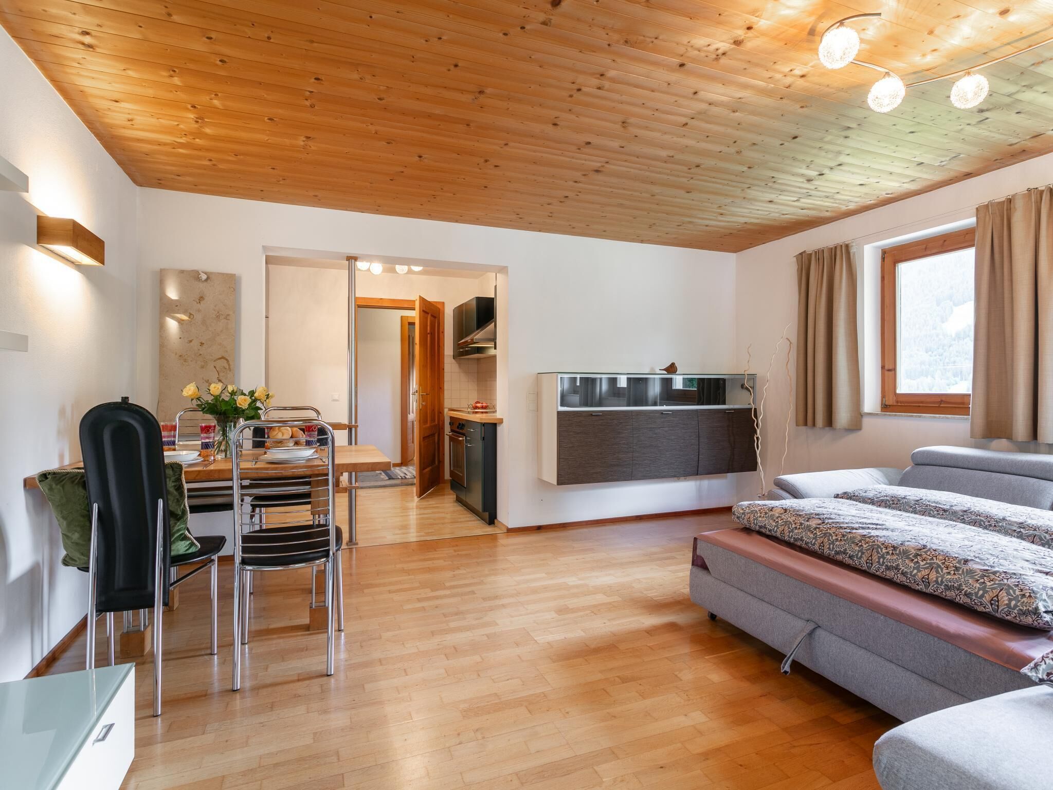 A modern interior with a wooden ceiling, a dining area with a table and chairs, a sofa, and a kitchen area.