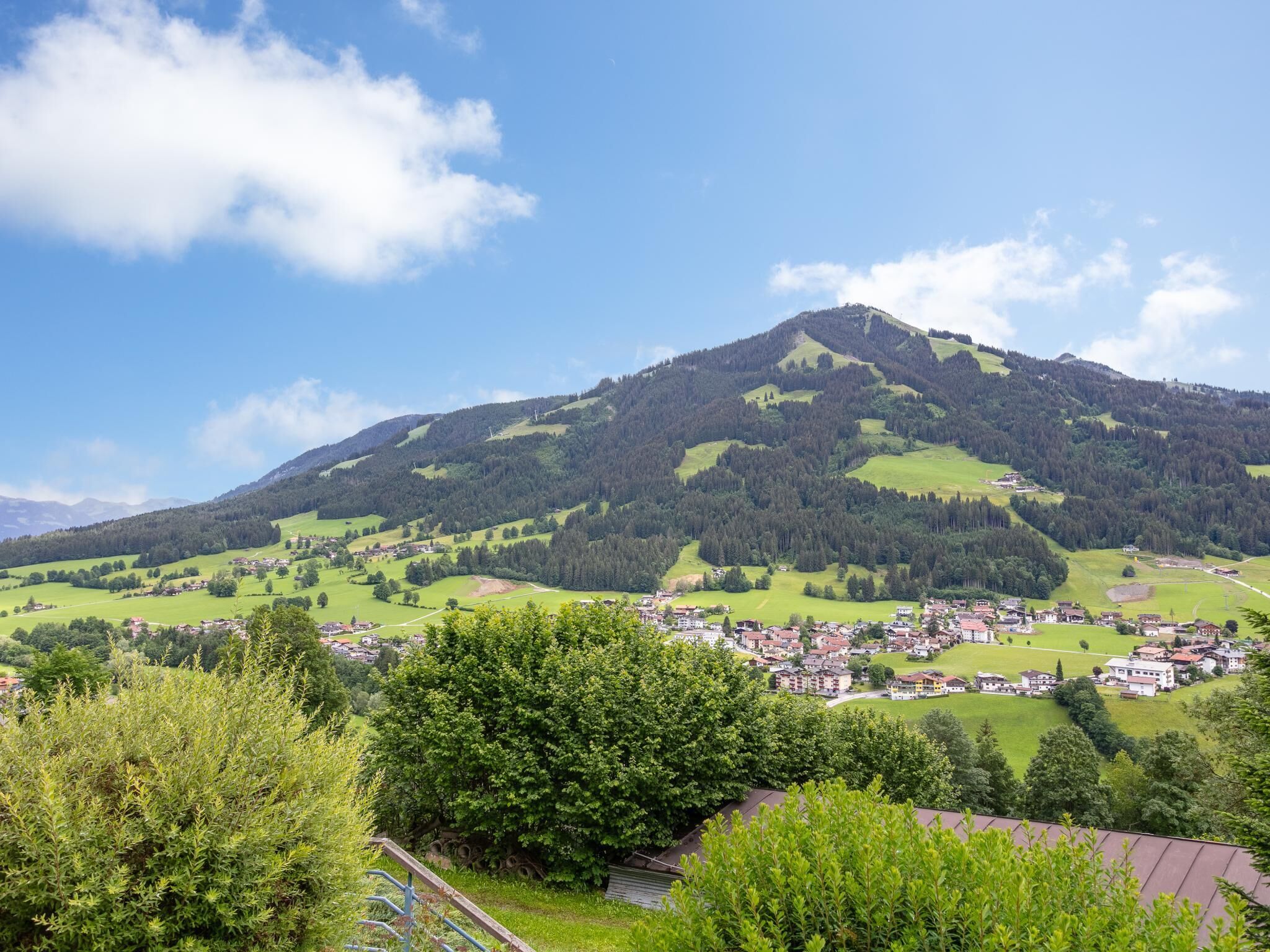 Ein Berg mit einem Dorf am Fuße, umgeben von Grün und blauem Himmel.