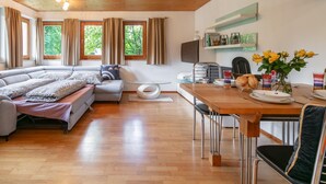 A modern living room with a sofa, dining table, and a view of greenery through windows. - Stylish vacation apartment with terrace (Westendorf)