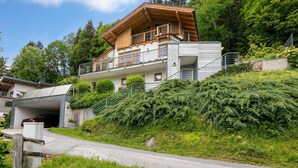 A modern two-story house with a wooden balcony, a garage, and a hillside garden. - Stylish vacation apartment with terrace (Westendorf)