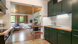 A modern kitchen with green cabinets, a wooden dining table, and a built-in oven. - Stylish vacation apartment with terrace (Westendorf)
