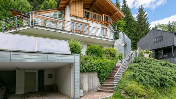 A multi-story building with a wooden balcony, a garage, and a staircase leading to a second level. - Stylish vacation apartment with terrace (Westendorf)