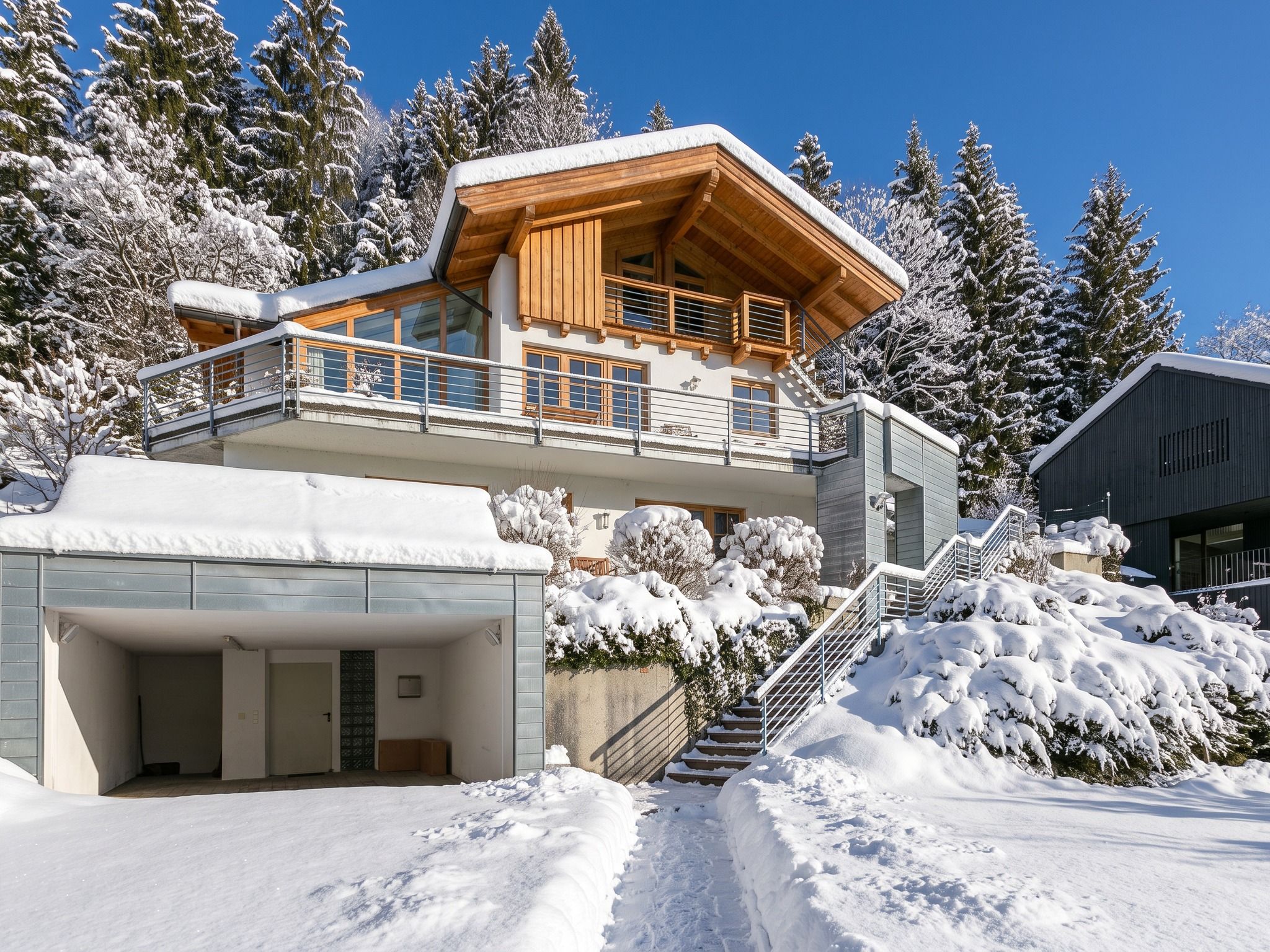 A modern chalet with a wooden exterior, a balcony, and a covered garage.