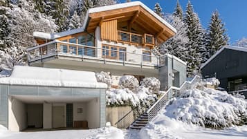 Ein modernes Chalet mit Holzausside, einem Balkon und einer überdachten Garage.