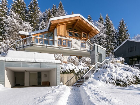 A modern chalet with a wooden exterior, a balcony, and a covered garage.