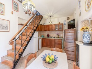 Una cocina con armarios de madera, salpicadero de azulejos, una mesa de comedor con un centro de frutas y una escalera con barandilla de metal.