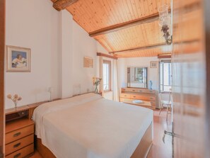 A bedroom with a wooden ceiling, a bed, a dresser, a mirror, and a window. - Charming house with a Stunning Panoramic Terrace (Marciana)