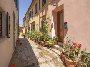 A narrow cobblestone street lined with traditional buildings, potted plants, and a wooden door. - Charming house with a Stunning Panoramic Terrace (Marciana)