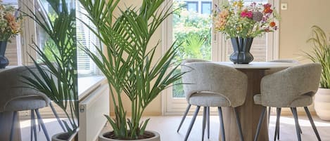 A dining area with a table, chairs, a potted plant, and a hanging light fixture.