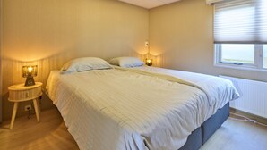 A bedroom with a bed, bedside lamps, a window with blinds, and a radiator.