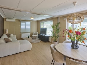 Een moderne woonkamer met een bank, een eettafel met stoelen, een televisie en een potplant.