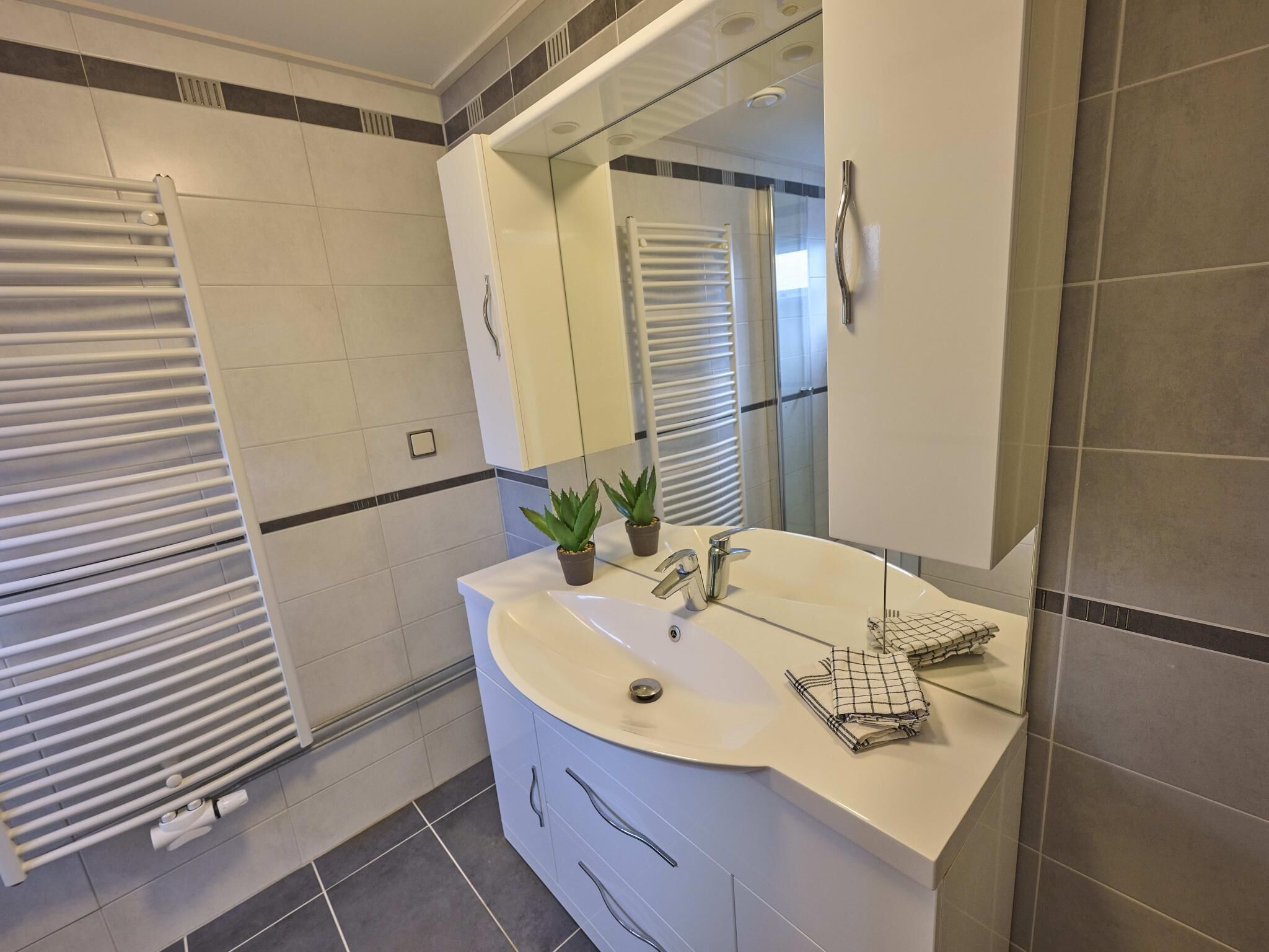 A modern bathroom with a white sink, a mirror, a towel rack, and a potted plant.