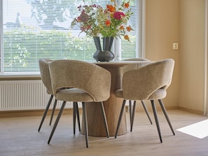 A dining area with a round wooden table, four woven chairs, and a vase of flowers.