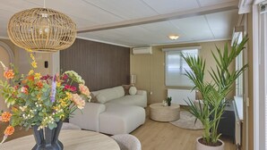 A modern living room with a sofa, a round table with a vase of flowers, a potted plant, and a hanging light fixture.