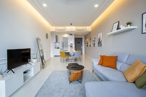 A modern living room with a flat-screen TV, sofa, coffee table, and dining area with chairs. - Beacon EXecutive Suite by Penang (George Town)