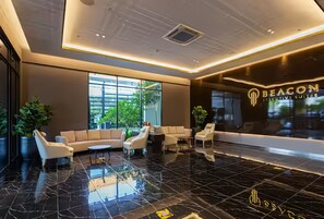A modern lobby with a black marble floor, a beige sofa, white armchairs, and a reception desk with 'BEACON EXECUTIVE SUITES' signage. - Beacon EXecutive Suite by Penang (George Town)