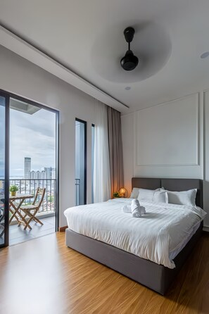 A modern hotel room with a large bed, a balcony with a view of the city, and a ceiling fan. - Beacon EXecutive Suite by Penang (George Town)