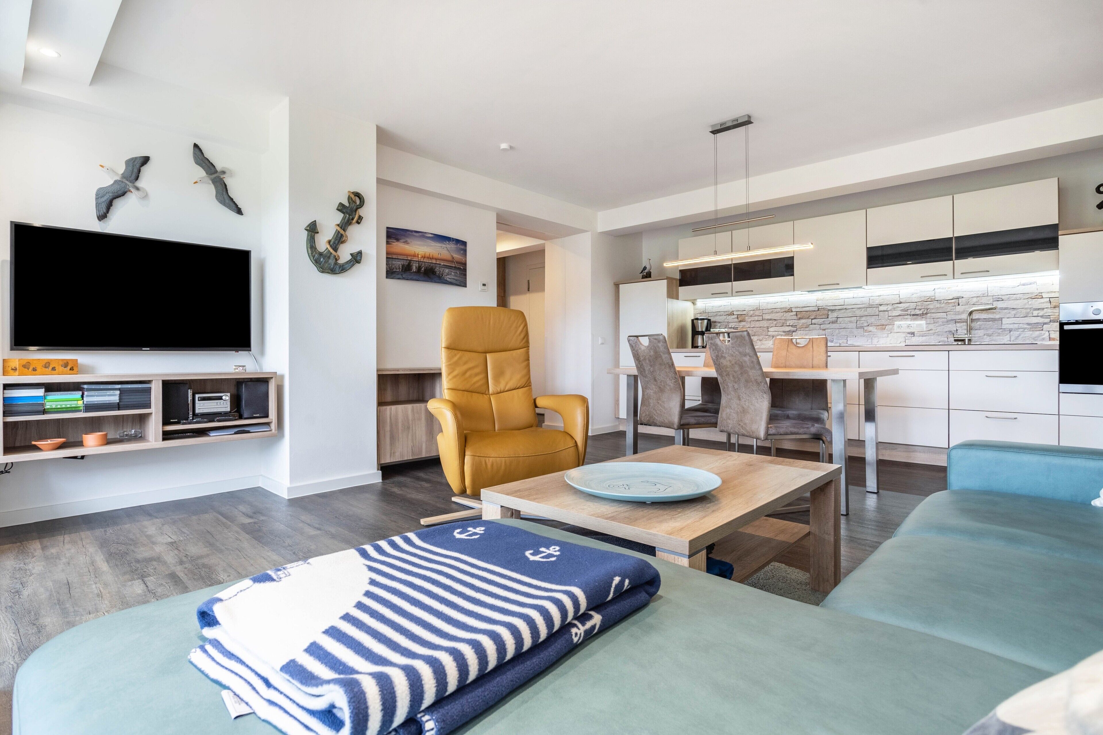 A modern living room with a TV, seating, and a kitchen in the background.