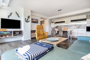 A modern living room with a TV, seating, and a kitchen in the background.