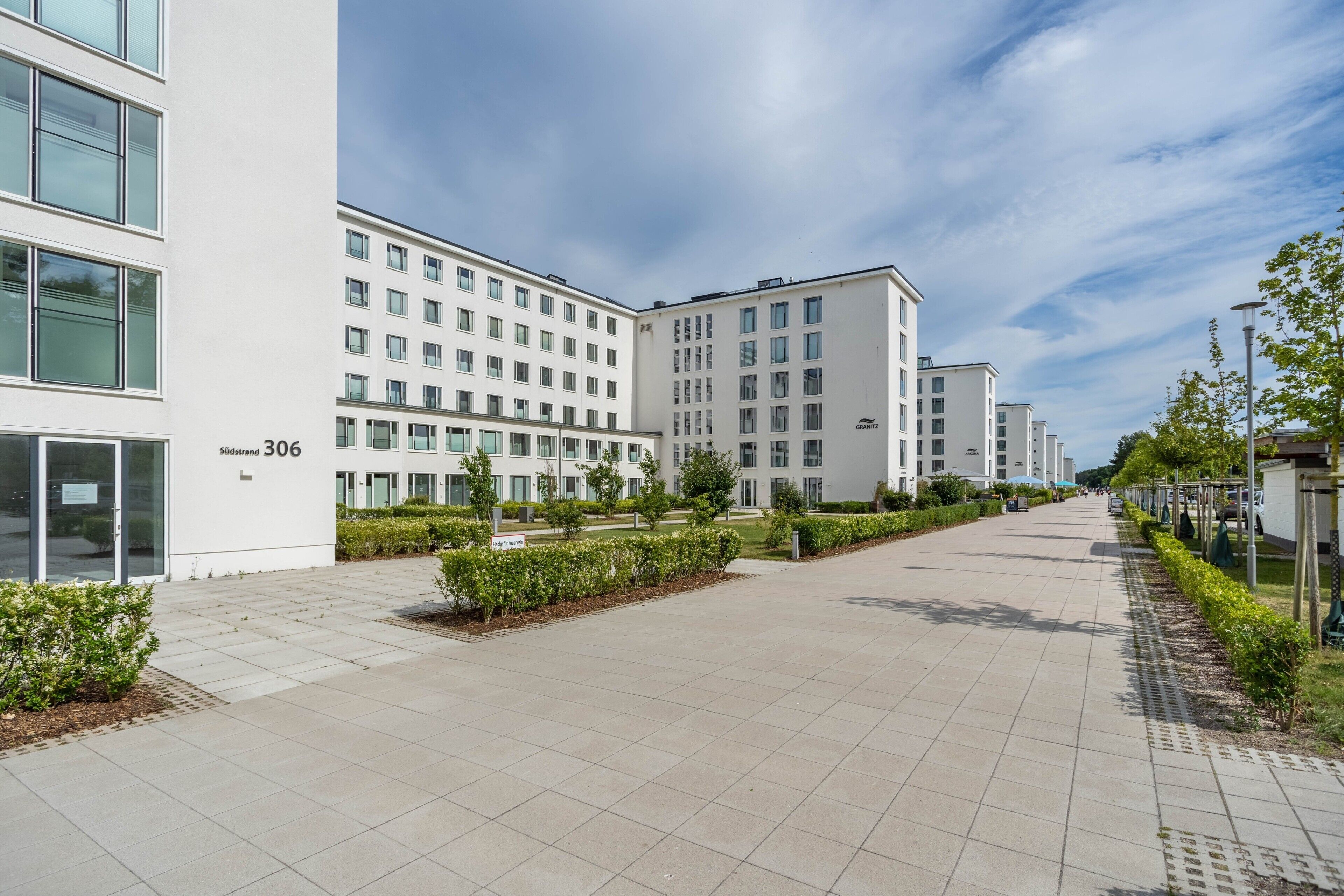 Ein modernes Gebäude mit flacher Fassade, Hausnummer 306, und einem gepflasterten Weg mit Grünflächen.