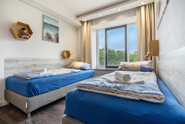 A modern bedroom with two beds, a large window, and a painting on the wall.